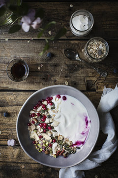 Breakfast on wooden table: yogurt with oat flakes, seeds, pistachios, hazelnuts and currants.
