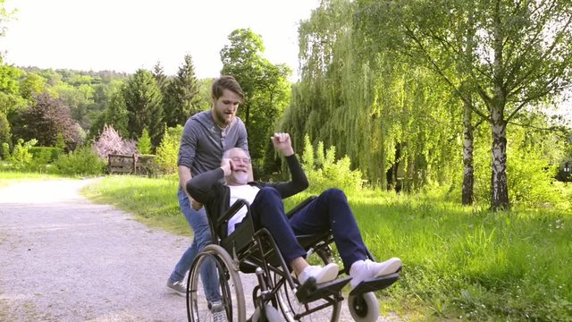 Son with disabled father in wheelchair in the park.