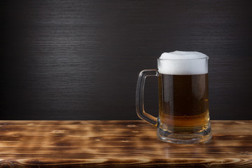 Mug of beer on wood surface. Dark background.