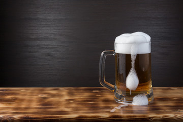 Mug of beer on wood surface. Dark background.