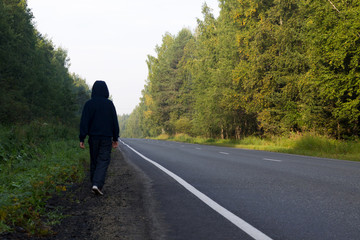 A boy walks along the roadside in a beautiful forest