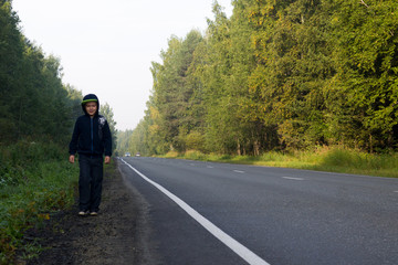 Obraz premium A boy walks along the roadside in the forest
