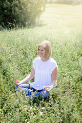 Happy woman is doing yoga in the meadow