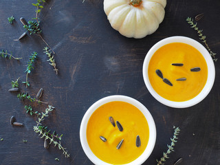 Two white bowls of pumpkin soup ornamental pumpkin adn thyme  on wooden table,