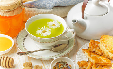 Green tea in a cup on a background of dry leaves of floral tea in a composition with accessories on a white background