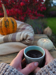 A woman holding a cup of coffe with the ornamental pumpkin, candle and blanket on backgroung.