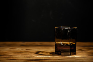 Old scratched glass of scotch whiskey on a wooden table. With place for your text.