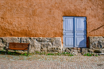 Fototapeta na wymiar An ancient textured wall with a stone basement, a blue door and a bench. Bright concept.