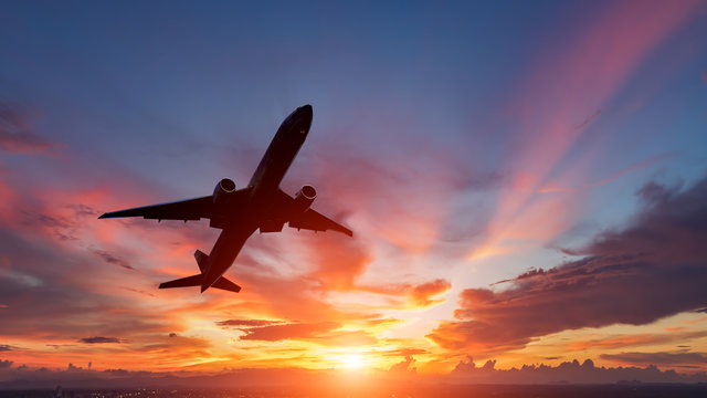 Fototapeta The silhouette of a passenger plane flying in sunset.