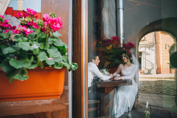 Look at wedding couple drinking coffee behind the doors in a cafe