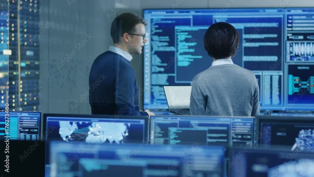 Poster in the system control room it specialist and project engineer have discussion, they're surrounded by