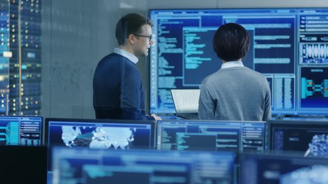 In the System Control Room IT Specialist and Project Engineer Have Discussion, they're surrounded by Multiple Monitors with Graphics.  Shot on RED EPIC-W 8K Helium Cinema Camera.