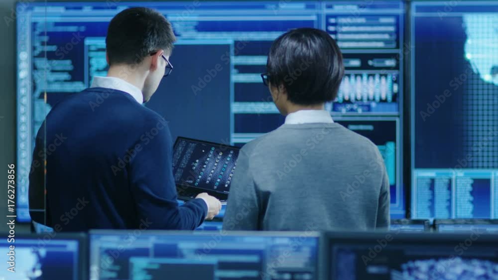 Poster in the system control room it specialist and project engineer have discussion, they're surrounded by