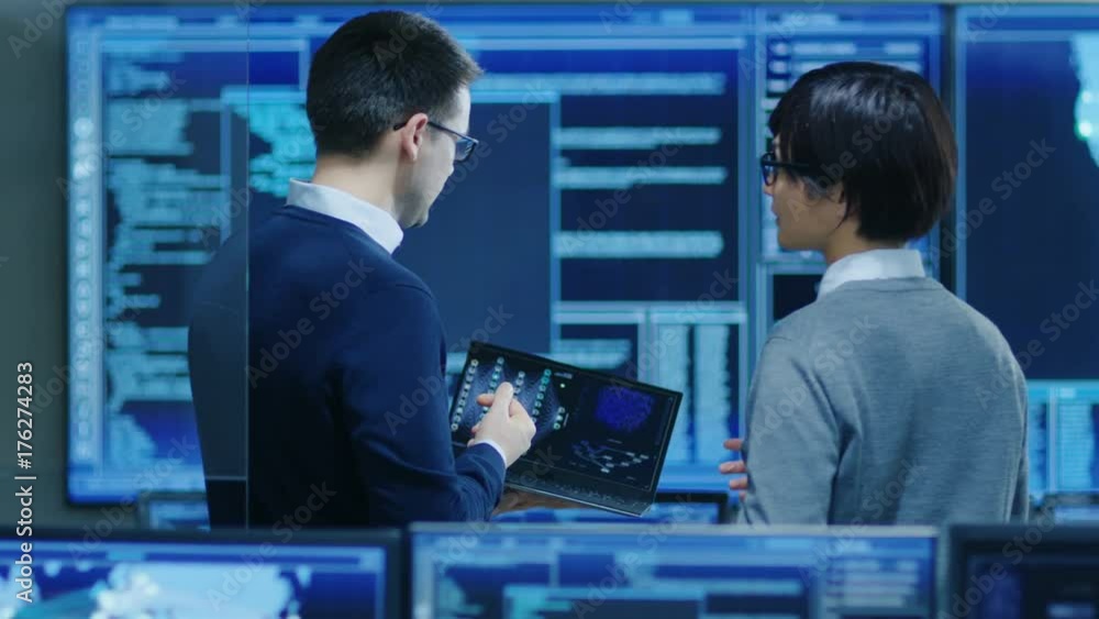 Poster in the system control room it specialist and project engineer have discussion while holding laptop, 