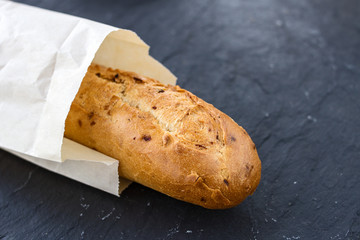 French appetizing fresh crispy fried golden baguette with onions in a craft package on a black graphite background.