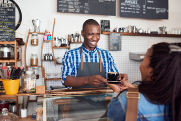 Smiling young barista handing coffee to a cafe customer