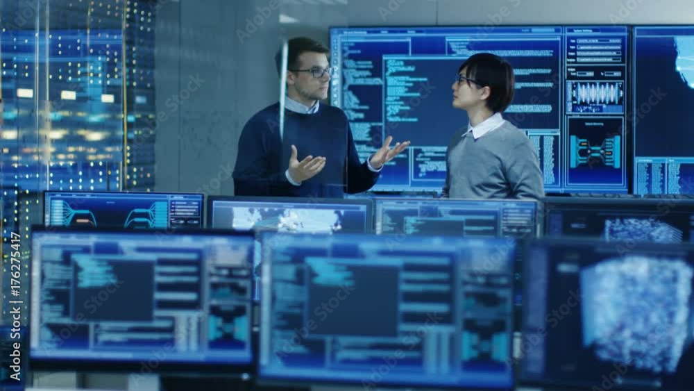Poster In the Data Center System Control Room Monitors Show Work Done on Neural Networking, AI integration and Data Mining. In the Background Two Specialists Talking.