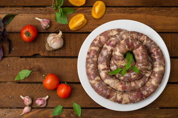 Raw fresh sausages in a white plate on a wooden background. Top view. Close-up