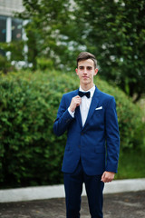 Portrait of a fashionable and stylish high school graduate in elegant tuxedo posing outdoor with bushes on the background.