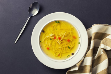 Tasty chicken soup in a ceramic soup dish and stripped kitchen towel on a black background