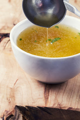 Pouring chicken soup into a bowl with a lade