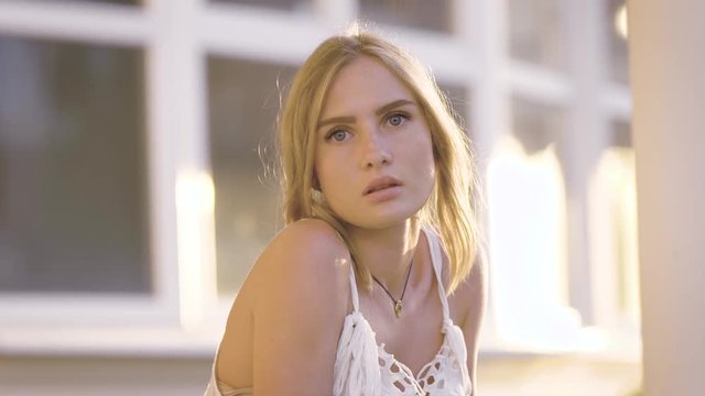 Portrait of sensual woman in white dress looking at camera with slight provocation at street.