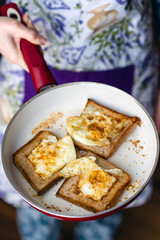The girl holds toasts with eggs in a frying pan
