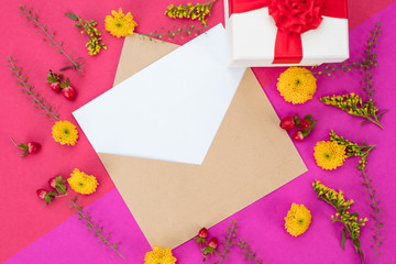 Romantic and colourful background of isolated blank card, envelope, yellow flowers and gift wrap with red bow. Copy space, top view