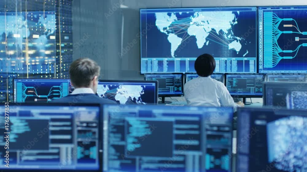 Fototapete In the System Control Room Operator and Administrator Sitting at Their Workstations with Multiple Displays Showing Graphics and Logistics Information. Shot on RED EPIC-W 8K Helium Cinema Camera.