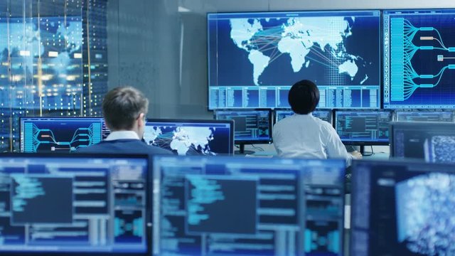 In the System Control Room Operator and Administrator Sitting at Their Workstations with Multiple Displays Showing Graphics and Logistics Information. Shot on RED EPIC-W 8K Helium Cinema Camera.