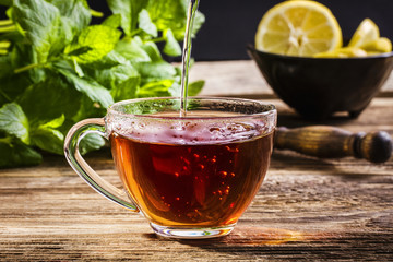 Pouring black tea into glass cup on a wooden table