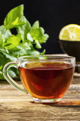 A cup of black tea on a wooden table with mint and lemon in the background