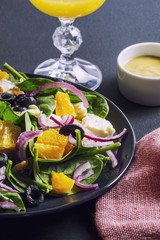 Salad with orange, spinach, red onion and olives on a dark table