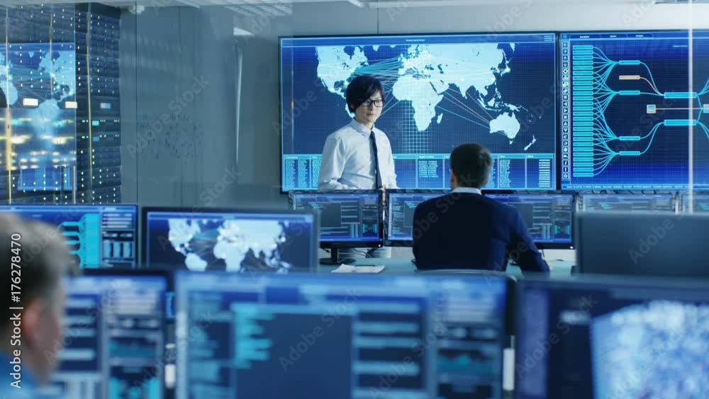 Poster In the System Control Room Chief Engineer Holds a Briefing for Member of the Staff. They're Work in Data Center and are Surrounded by Multiple Screens Showing Maps, Logistics Data. 