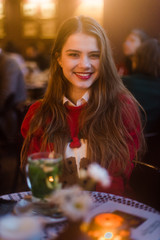 Beautiful young girl with makeup and hairstyle sitting in restaurant.