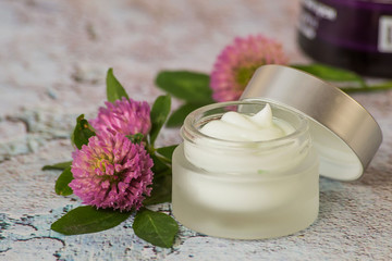   Natural cosmetic. A small glass jar with cream for skin care face and fresh clover flowers on a light background. 