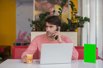 Smiling businessman talking at phone with laptop beside at the cafe