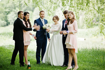 Wedding couple, bridesmaids and groomsmen drinking champagne on a festive wedding day in the park.