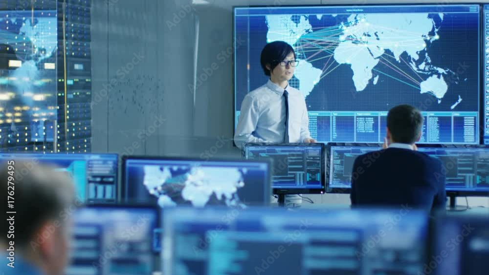 Poster In the System Control Room Manager Holds a Briefing for His Staff Member. They're Work in Data Center and are Surrounded by Multiple Screens Showing Maps, Logistics Data. 