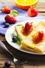 Homemade crepes with strawberries and jam on a wooden table