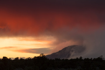 View of distant Pine Valley mountain at sunset with the wind blowing the storm away and trees silhouetted in the foreground