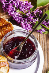 Cherry jam in a glass, croissant, lilac on a wooden rustic table