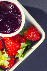 Strawberry jam and strawberries in a square bowl on a dark stone table