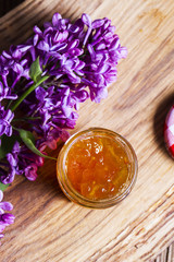 A jar of orange jam and lilac on a wooden table, top view