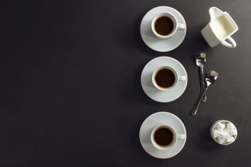 Three cups of coffee, sugar, milk on a dark background, space for text