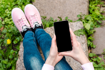 close up white mobile phone in fashionable, trendy woman hands on the background of green grass with paving stone