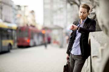 Caucasian businessman waiting outside and looking at his watch.