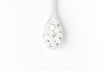 Pills on the spoon and scattered on the white surface