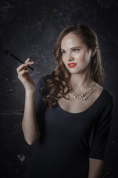 Female in a bad mood and grinning. Noir film style woman in dress holding black pen. Studio shot. Old fashion photo
