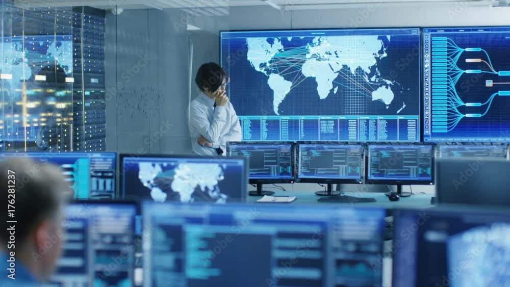 Poster In the System Control Room Chief Engineer Thinks While Standing Before Big Screen with Interactive Map on it. Data Center is Full of Monitors Showing Graphics. 